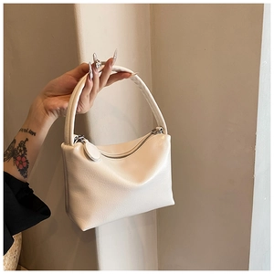 Detailed close-up of cream textured faux leather handbag with silver zip and round charm