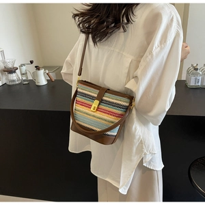 Detail view of woven bucket bag with colorful stripes and brown leather trim on a model