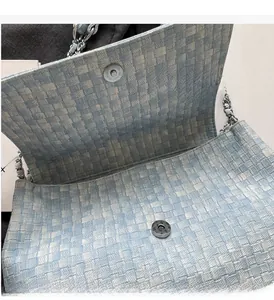 Detail of silver magnetic buckle and woven texture on a light blue chain tote bag