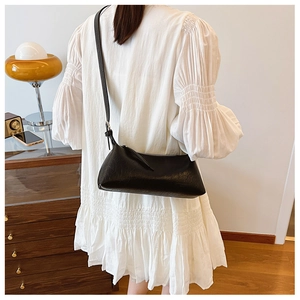 Minimalist black baguette bag with textured leather and metal zipper detail on model