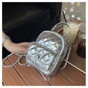 Close-up of a silver quilted mini backpack with chain strap and twist-lock on a wooden table