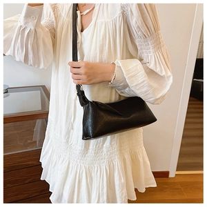 Detail of black textured leather baguette bag with adjustable strap and metal hardware