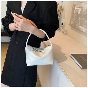 Polished white leather shoulder bag with circular charm shown on a stylish model