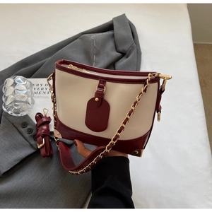 Close-up of contrast bucket bag with metal chain and burgundy leather strap detail