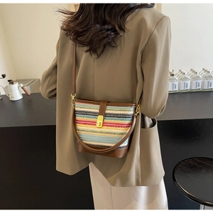 Close-up of colorful woven bucket bag featuring brown leather trim and golden clasp
