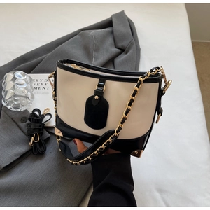 Detail of contrast color handbag featuring gold chain strap and reinforced metal corners