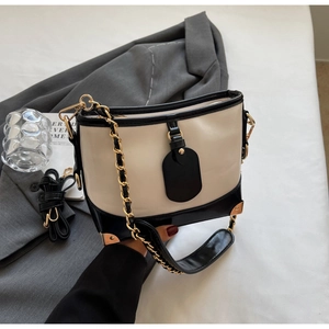 Close-up of contrast bucket bag with chain strap and gold corners on a grey blazer