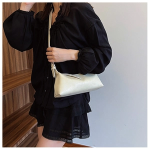 Detailed view of white textured leather shoulder bag worn on shoulder by model