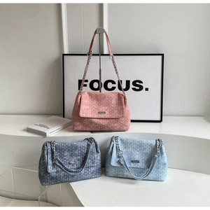 Detailed view of woven tote bags in pink, dark blue, and light blue with chain straps