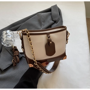 Detail of color-block bucket bag with vintage metal corners and golden chain strap