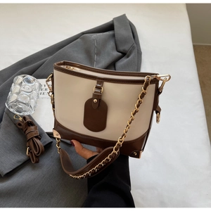 Detail of color-block bucket bag with golden corner guards and adjustable leather straps