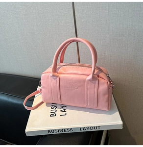 Pink Boston bag with KS&KS embossed text shown on decorative book props and textured wall