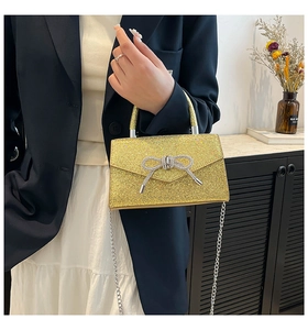 Close-up of glittery gold evening bag featuring a rhinestone bow and chain strap