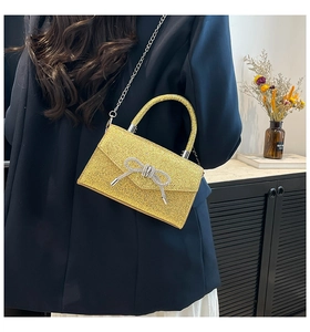 Detail of golden sequin evening bag featuring a silver metal chain and rhinestone bow