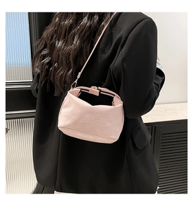 Détail du sac bandoulière en cuir rose avec fermoir doré sur un blazer noir