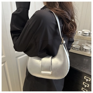 Detail of silver metallic crescent shoulder bag with golden hardware and flap design