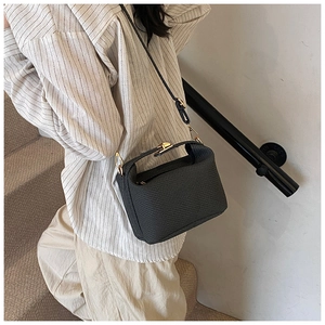 Détail d'un sac à bandoulière en cuir gris avec fermoir doré porté par un mannequin