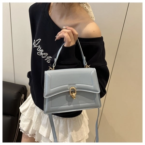 Dettaglio della borsa in pelle azzurra con fibbia dorata indossata da una modella