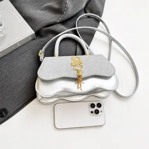 Silberne Wellenhandtasche mit Glitzer und Goldquaste neben einem Smartphone gezeigt