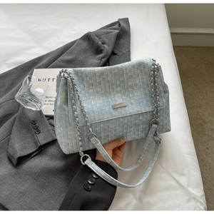 Close-up of blue and white tweed tote bag with silver chain strap and metal logo plate