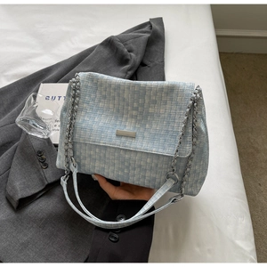 Detail of light blue woven tote bag with silver chain strap on grey blazer background