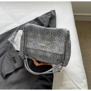 Detail of grey woven texture crossbody bag featuring silver chain strap and metallic clasp