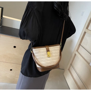 Detail of colorful woven straw bucket bag with brown leather trim and golden twist-lock