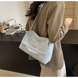 Side view of a light blue woven tweed tote bag with a chain strap on a model