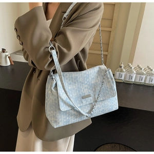 Detail of light blue tweed tote bag with silver chain strap and metal flap hardware