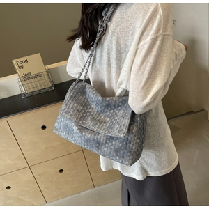 Detail of grey woven tote bag with metallic chain strap worn by model in minimalist setting