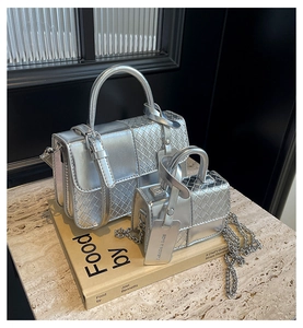 Detail showing two silver metallic handbags with woven textures on marble surface