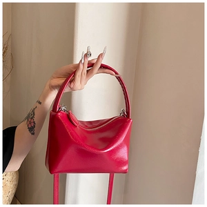 Detail of red faux leather handbag featuring thick cylindrical handle and silver zipper