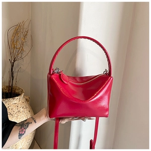 Detail view of glossy red patent leather handbag featuring curved handle and zip closure