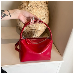 Detailed close-up of glossy red leather handbag with metallic zipper and curved handle