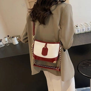 Chic two-tone burgundy and cream bucket bag with gold chain strap shown on a model