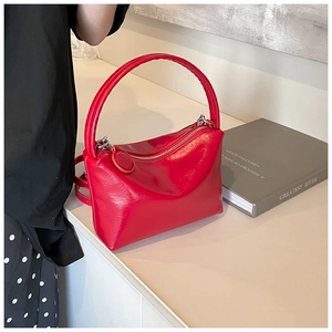 Close-up of vibrant red glossy handbag with round handle and silver zipper on light surface