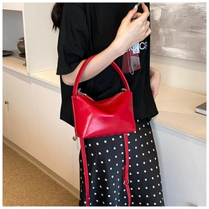 Detailed view of a bright red glossy leather trapezoid crossbody bag with silver hardware