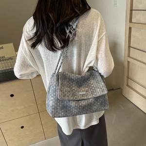 Blue woven tote bag with silver chain strap shown worn by a model in a modern room
