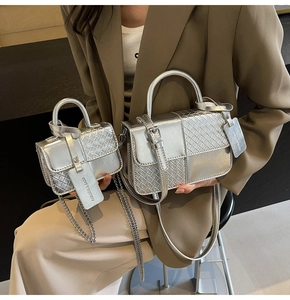 Macro detail of the silver woven texture and metallic finish on two sizes of square handbags