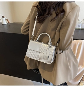 Detail of silver woven textured crossbody bag featuring side hanging logo tag and strap