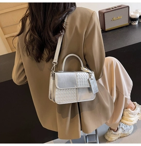 Silver woven crossbody bag with metallic finish and metal tag on a brown suit background