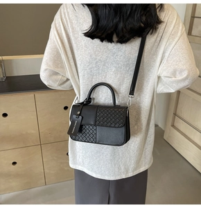 Detail of black crossbody bag featuring woven texture panel and silver hardware on a model