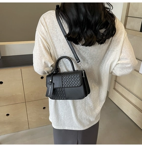 Crossbody view of black textured handbag with woven pattern and leather strap detail