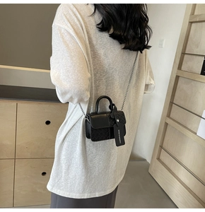 Detail of black leather handbag with woven texture, silver chain, and fashion tag