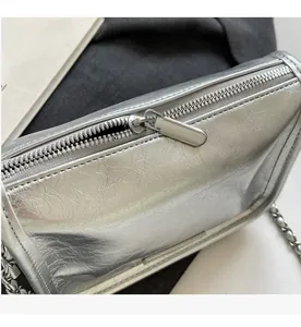 Détail d'un sac argenté brillant avec bandoulière chaîne et fermeture éclair fluide