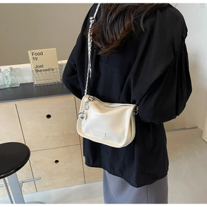 Détail d'un sac à bandoulière blanc crème brillant avec chaîne et breloque argentée