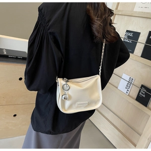 Détail du sac minimaliste en similicuir crème avec chaîne argentée et breloque boule
