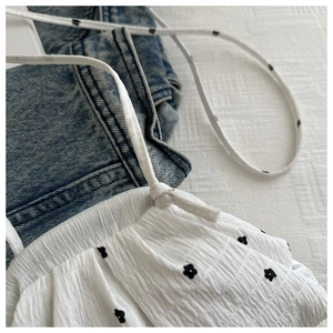 Détail du tissu blanc froncé avec broderie florale noire et fines bretelles de la robe