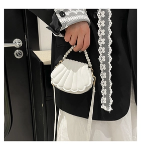 Detail of shell-shaped white handbag featuring a pearl handle and scalloped stitching