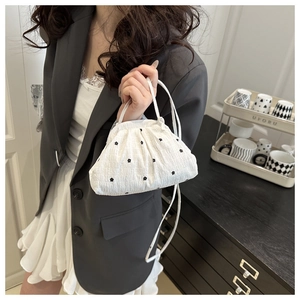 Détail du sac blanc froncé avec broderie florale noire sur un tissu texturé et élégant